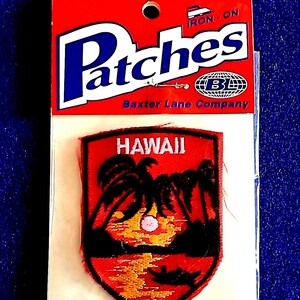 May include: Iron-on patch featuring a red, black, and gold Hawaiian sunset design. The patch is in a shield shape and includes the word "HAWAII". The packaging reads "Patches" and "Baxter Lane Company".