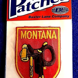 May include: Iron-on patch featuring a red shield with "MONTANA" in gold lettering. The patch depicts a brown saddle and rope. The patch is packaged with a red and white header that reads "Patches" and "Baxter Lane Company."