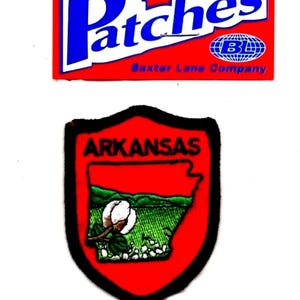 May include: Two patches are displayed. The top patch is a red rectangle with the word "Patches" in blue and white lettering. The bottom patch is a red shield with the word "ARKANSAS" and a landscape design.
