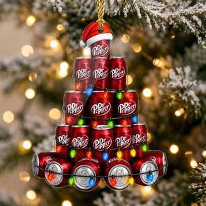 May include: A Christmas tree-shaped ornament featuring a stack of red Dr Pepper soda cans. The cans are arranged in a pyramid, topped with a Santa hat, and wrapped in a string of colorful miniature Christmas lights with visible bulbs.