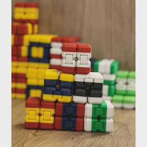 May include: A collection of colorful, interlocking toy blocks in various arrangements. The blocks are primarily red, yellow, blue, white, black, and green, creating a visually engaging display. The blocks are stacked on a wooden surface.
