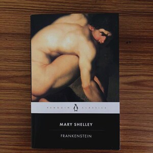 May include: A Penguin Classics edition of Mary Shelley's "Frankenstein" book. The cover features a painting of a nude figure. The book has a black cover with white text and a white band with the Penguin logo.