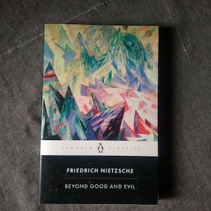 May include: A paperback book titled "Beyond Good and Evil" by Friedrich Nietzsche. The book cover features a colorful abstract painting with a mountain theme. The Penguin Classics logo is visible.