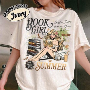 May include: Ivory t-shirt featuring a graphic of a woman reading a book, stacked books, and the words "BOOK GIRL SUMMER." The shirt also features the text "Girls Just Wanna Have Sun!" and "Dive Into A Good Book!"