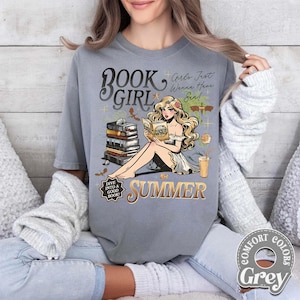 May include: A grey t-shirt with a graphic of a woman reading, the words "BOOK GIRL SUMMER", and the text "Girls Just Wanna Have Sun!". The design includes books, a drink, and the text "Dive into a good book!"