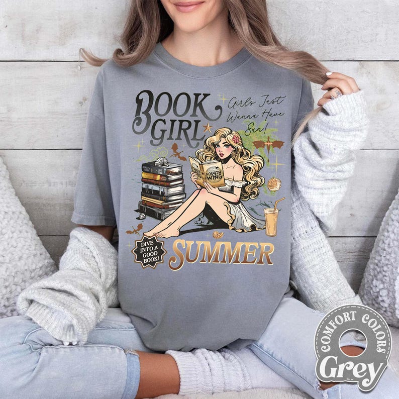 May include: A grey t-shirt with a graphic of a woman reading, the words "BOOK GIRL SUMMER", and the text "Girls Just Wanna Have Sun!". The design includes books, a drink, and the text "Dive into a good book!"