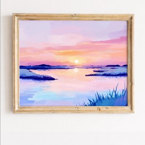 以下が含まれることがあります： 水面上の夕焼けを描いた額入りの水彩画。空はピンクからオレンジ色に変わり、地平線に沈む太陽。水面は空の色を映し出し、手前には青い草が描かれています。