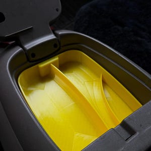 Puede incluir: Un organizador de consola central amarillo brillante, hecho a medida para la consola central de un vehículo. El organizador es de plástico y tiene múltiples compartimentos y divisores. La consola es gris.