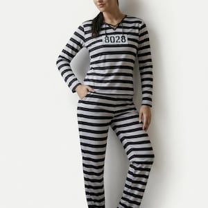 Könnte beinhalten: Ein schwarz-grau gestreiftes Gefängniskostüm, bestehend aus einem langärmeligen Oberteil, einer Hose und einer passenden Mütze. Das Oberteil hat ein Etikett mit der Nummer "8028". Dieses Outfit ist eine klassische Wahl für Halloween oder Kostümpartys.