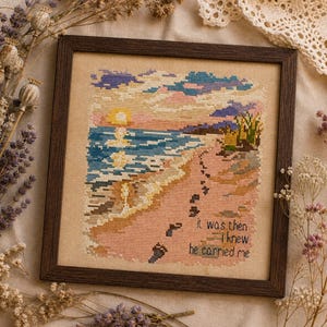 May include: A square cross-stitch embroidery in a dark brown wooden frame depicting a beach scene at sunset with a yellow sun, blue ocean waves, and pink sand. A trail of dark footprints leads across the sand with the text, It was then I knew he carried me.