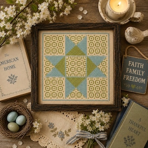 May include: A square cross-stitch embroidery featuring a geometric star pattern in shades of light blue and olive green on a beige fabric background, encased in a dark brown wooden frame. The design consists of a central star surrounded by grid motifs.