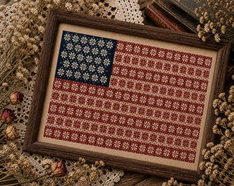 Könnte beinhalten: Eine gerahmte Kreuzstichstickerei, die die amerikanische Flagge darstellt, wobei die Sterne und Streifen durch ein sich wiederholendes Muster aus kleinen, cremefarbenen Schneeflockenmotiven auf einem dunkelblauen Feld und dunkelroten Streifen ersetzt sind.