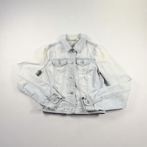 May include: A light-wash denim jacket featuring a classic collar, long sleeves with buttoned cuffs, and a front button closure. The garment includes two chest pockets with buttoned flaps and subtle distressed detailing throughout the fabric.