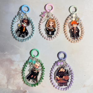 Può includere: Cinque portachiavi circolari di perline con personaggi in stile chibi. Ogni portachiavi presenta un anello in plastica colorata, un cerchio di piccole perline e un ciondolo centrale in acrilico che raffigura un personaggio in divisa.