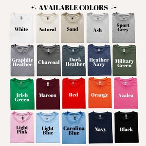 May include: A display of folded t-shirts in various colors, including white, natural, sand, ash, sport grey, graphite heather, charcoal, dark heather, heather navy, military green, irish green, maroon, red, orange, azalea, light pink, light blue, carolina blue, navy, and black. Text reads "AVAILABLE COLORS."