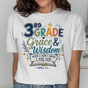 Może przedstawiać: Biała koszulka z kolorowym wzorem graficznym. Projekt zawiera słowa "3rd Grade Grace & Wisdom" z tekstem "When I don't know, I ask God. James 1:5". Projekt przedstawia gwiazdę, serca i otwartą książkę.