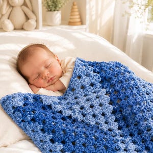 May include: A baby is sleeping while covered by a handmade crochet blanket featuring a gradient of blue yarn colors. The blanket displays a classic granny square stitch pattern that transitions from light blue to deep navy blue across the fabric.