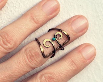 May include: A gold-toned ring with a turquoise stone and a unique, intricate design. The ring is worn on the middle finger of a hand.
