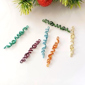 May include: A collection of colorful wire ornaments in green, purple, blue, orange, and gold. The ornaments are in a spiral shape. A Christmas tree branch and a red ornament are in the background.