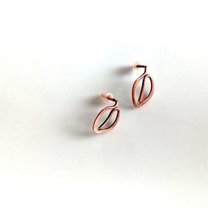 May include: A pair of copper-coloured wire earrings. Each earring has a stylised leaf shape with a delicate, open design. The earrings have a post backing for pierced ears. The earrings are displayed on a white background.