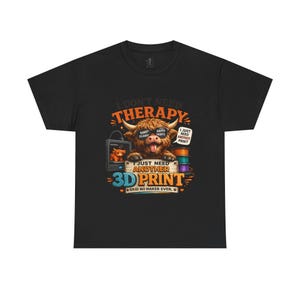 Op de afbeelding: Zwart t-shirt met een kleurrijke afbeelding van een Schotse hooglander met een zonnebril. De tekst luidt: "Ik heb geen therapie nodig, ik heb gewoon nog een 3D-print nodig." Het ontwerp bevat een 3D-printer en stapels filament.