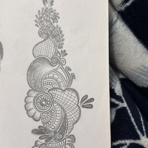 May include: A graphite pencil drawing on white paper featuring an intricate henna-style pattern. The design consists of a vertical arrangement of paisley shapes, floral motifs, cross-hatched shading, and delicate leaf-like elements in gray.