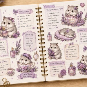 以下が含まれることがあります： ハムスター、ラベンダー、「Today's Plan」、「Tea Time」などのテキストが描かれたイラストステッカーが貼られた、開いたスパイラル綴じのジャーナル。 ステッカーはソフトな紫とクリームの色合いです。