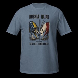 May include: A pale blue t-shirt with a graphic of a wolf and an oryx facing each other, with the text "BOSNIA | QATAR" above and "JUNE 24, 2020 SEATTLE - LUMEN FIELD" below. The wolf is colored with the Bosnian flag, and the oryx with the Qatar flag.