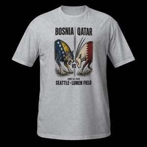 May include: A light grey t-shirt with a graphic depicting a wolf and an antelope, symbolising Bosnia versus Qatar. The text "BOSNIA | QATAR" and "JUNE 24, 2026 SEATTLE - LUMEN FIELD" are printed above and below the illustration.