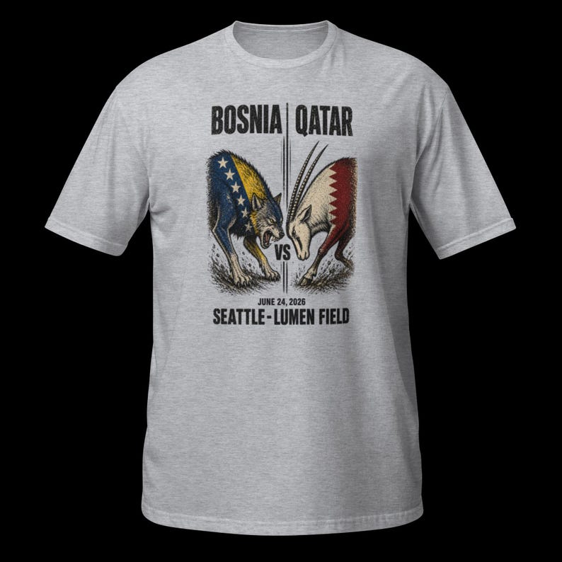 May include: A light grey t-shirt with a graphic depicting a wolf and an antelope, symbolising Bosnia versus Qatar. The text "BOSNIA | QATAR" and "JUNE 24, 2026 SEATTLE - LUMEN FIELD" are printed above and below the illustration.