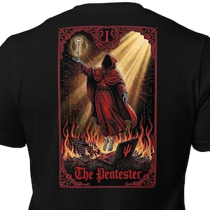 May include: Black t-shirt featuring a graphic of a robed figure holding a key, with flames and the text "The Pentester." The design is framed in red, with a mystical theme.