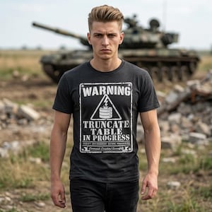 May include: Dark gray t-shirt with a white warning sign graphic. The sign reads "WARNING TRUNCATE TABLE IN PROGRESS" with a lightning bolt and database symbol. The shirt is worn by a person in front of a tank.