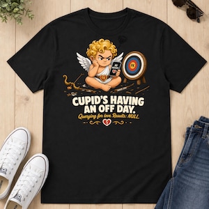 Könnte beinhalten: Ein schwarzes T-Shirt mit einer Grafik eines frustrierten Cupido mit blondem Haar und weißen Flügeln, der ein Handy mit der Aufschrift "NO MATCHES" und einem gebrochenen Herzen hält. Text: "CUPID'S HAVING AN OFF DAY. Querying for love. Results: NULL."