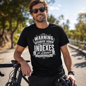 May include: A black short-sleeved t-shirt featuring white text that reads WARNING DATABASE ADMIN MAY DISCUSS INDEXES at Dinner you've been warned, accompanied by two small database cylinder icons and decorative scrollwork elements.