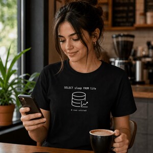 May include: A black short-sleeved t-shirt featuring a white graphic print of a database icon with an upward trend line. Above the icon is the text "SELECT sleep FROM life" and below the icon is the text "8 rows returned" in a simple font.
