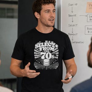 Może przedstawiać: Czarny t-shirt z krótkim rękawem z białym nadrukiem graficznym o treści SELECT FROM THE 70s, ORDER BY FUNK DESC, ze stylizowaną ikoną bazy danych, gwiazdkami i promienistymi liniami umieszczonymi na środku klatki piersiowej.