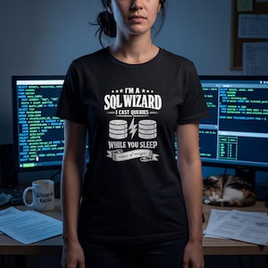 Op de afbeelding: Zwart t-shirt met de witte tekst "I'M A SQL WIZARD I CAST QUERIES WHILE YOU SLEEP rows of magic". Het ontwerp bevat databasesymbolen en bliksemschichten. Het t-shirt wordt door een persoon gedragen.