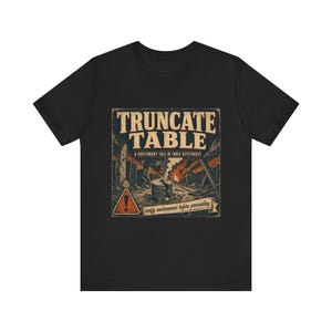 May include: Black t-shirt with a graphic design featuring the words "TRUNCATE TABLE" in a vintage style. The design includes an illustration of a hazardous environment with a warning sign and the text "verify environment before proceeding."