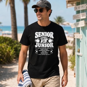 May include: A black short-sleeved t-shirt featuring white graphic text that reads SENIOR VS JUNIOR, A TALE OF COFFEE AND CHAOS, Git Blame vs Google It, It Worked Yesterday vs Rewrite It, Calm vs Panic, Experience vs Energy, Both equally confused.