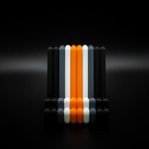 May include: A collection of colorful, cylindrical objects arranged vertically against a black backdrop. The objects alternate between black, gray, white, and orange, creating a visually striking pattern. The arrangement suggests a design or decorative element.