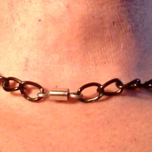 May include: A black chain necklace with a silver magnetic clasp. The necklace is worn around a person's neck.