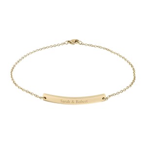 May include: A delicate gold-coloured bracelet with a chain design. The bracelet features a curved bar pendant engraved with the names "Sarah & Robert". The bracelet is a simple and elegant piece of jewellery.