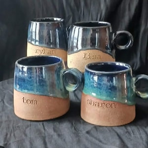 Peut inclure: Quatre tasses en céramique faites à la main avec un design unique. Les tasses présentent une palette de couleurs bicolores, avec une base marron et un dessus émaillé bleu et vert. Chaque tasse a une anse et un nom gravé sur la base : Rylan, Lisa, Tom et Sharon.