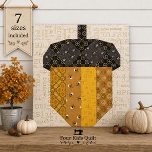 May include: A square quilt block featuring a central acorn design made of fabric strips in shades of yellow, gold, and brown. The acorn cap is dark grey with a floral pattern. The background is cream with text. A banner reads 7 sizes included.