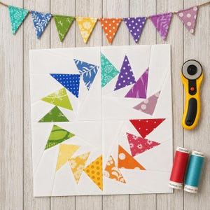 May include: A white quilt block with colorful triangles arranged in a spiral pattern. A yellow rotary cutter, red and teal thread spools, and a banner of small fabric flags are also present.