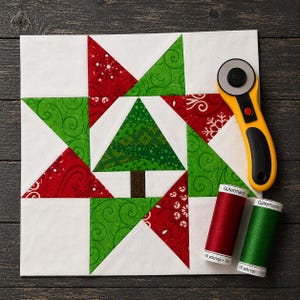Könnte beinhalten: Ein Weihnachtsbaum-Quiltblock mit rot-grün gemustertem Stoff, einem braunen Baumstamm und weißem Hintergrund. Ein gelber Rollschneider und zwei Garnrollen liegen neben dem Block. Die Garnrollen sind rot und grün.