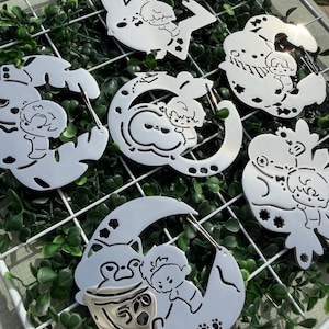 May include: A collection of six silver-toned metal carabiners, each featuring a unique cutout design of a small cartoon character interacting with various shapes like stars, moons, and animals, with a spring-loaded gate mechanism.