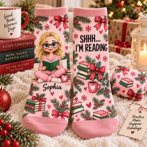 May include: A pair of light pink socks featuring a repeating pattern of green pine branches, red bows, hearts, and stacks of books. One sock displays a cartoon girl reading with the name Sophia, while the other reads SHHH... I'M READING.
