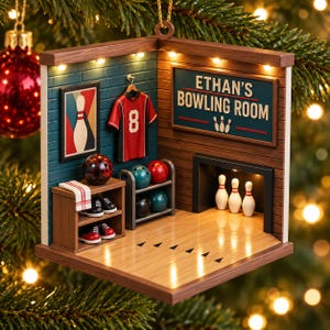 Op de afbeelding: Een miniatuur bowlingkamer ornament met een verlichte houten structuur, een bord met de tekst ETHAN'S BOWLING ROOM, een rood shirt met nummer 8, een rek met bowlingballen, een paar bowlingschoenen en drie witte kegels.