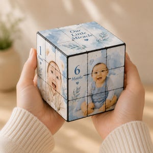 May include: A custom photo puzzle cube featuring blue watercolor accents and botanical illustrations. The cube displays photographs of an infant, the text "Our Little Miracle," and milestone markers including "1 Month" and "6 Months" with small blue hearts.